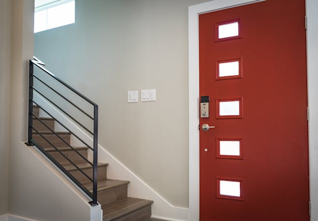 red front door and wooden stairs leading upstairs from the landing